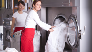 Smiling workers empty a washing machine in an industrial laundry equipped with an RFID system.